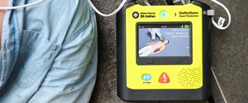 Resuscitation being performed on a patient, with an AED to the right of the frame